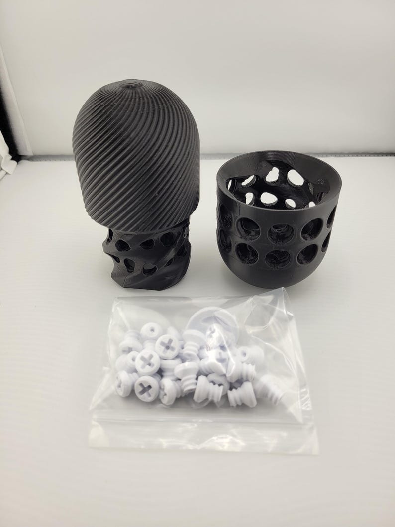 May include: A black 3D-printed sculpture with a skull-like base and a spiraling top, next to a perforated cup and a bag of white screws. The sculpture has a unique, textured design. The objects are on a white surface.