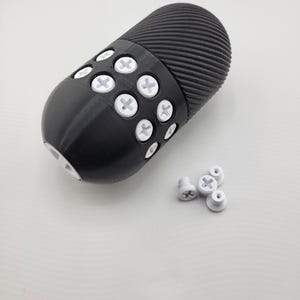 May include: A black, cylindrical object with a ridged top and a rounded bottom. The object has several white, cross-shaped accents. Several loose white accents are also present.