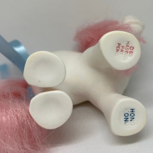 May include: White pony toy with pink hair, blue ribbon, and "HONG KONG" and "&copy;83 HASBRO PAT PEND" printed on the bottom.
