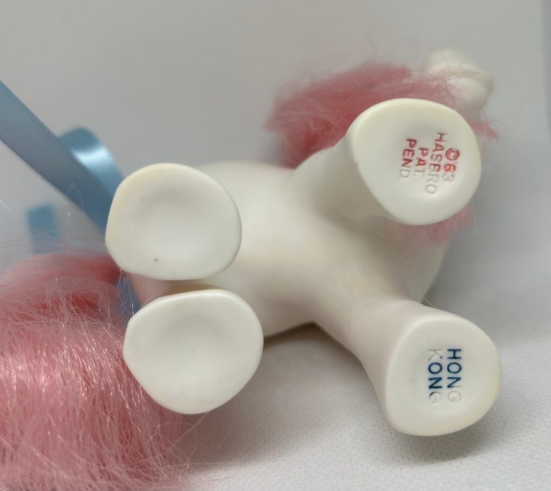 May include: White pony toy with pink hair, blue ribbon, and "HONG KONG" and "&copy;83 HASBRO PAT PEND" printed on the bottom.