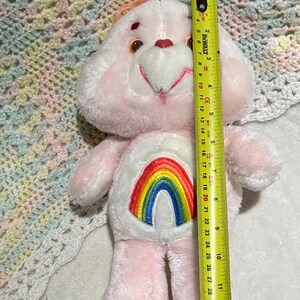 Puede incluir: Oso de peluche rosa con un arco&iacute;ris bordado en el pecho. El oso mide aproximadamente 50 cm de alto.