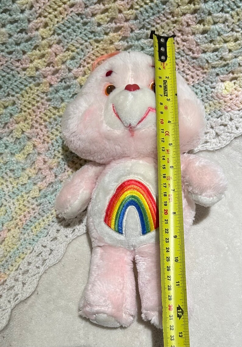 Puede incluir: Oso de peluche rosa con un arco&iacute;ris bordado en el pecho. El oso mide aproximadamente 50 cm de alto.