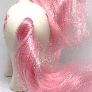 May include: A white pony with pink hair and a pink tail. The pony has a pink and white swirl pattern on its body.