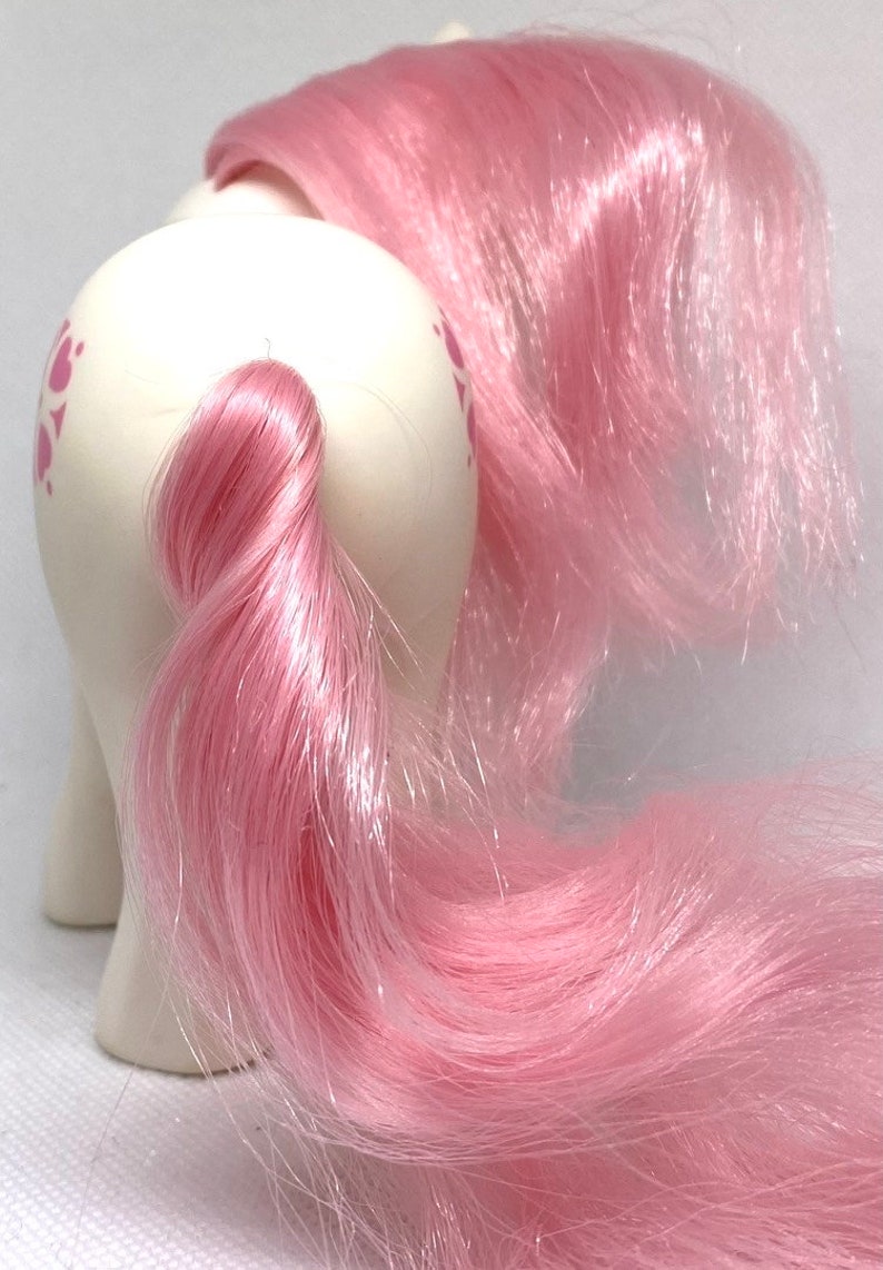 May include: A white pony with pink hair and a pink tail. The pony has a pink and white swirl pattern on its body.