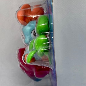 Puede incluir: Una bl&iacute;ster de pl&aacute;stico que contiene cuatro peque&ntilde;as figuras de pl&aacute;stico. Las figuras son de varios colores, incluyendo naranja, azul, verde y rosa. Las figuras est&aacute;n apiladas, con la figura naranja en la parte superior.