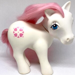 May include: White My Little Pony with pink hair and a pink flower symbol on its flank.