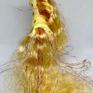 Puede incluir: Un caballo de juguete amarillo con una melena y una cola largas y fluidas. La melena y la cola est&aacute;n hechas de un material suave y esponjoso y tienen un brillo rosado. El caballo tiene manchas marrones en su cuerpo.