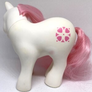 May include: White pony with a pink mane and tail. The pony has a pink and white flower design on its flank.