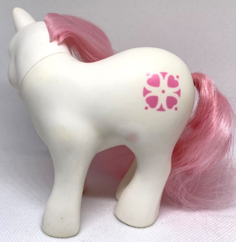 May include: White pony with a pink mane and tail. The pony has a pink and white flower design on its flank.