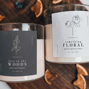 Puede incluir: Dos tarros de velas de vidrio con etiquetas. El tarro de la izquierda tiene una etiqueta gris oscuro con texto blanco que dice "YOUR CANDLE CO lost in the WOODS cedar/pine/bergamot 18 oz / 454 g / 80 hr". El tarro de la derecha tiene una etiqueta blanca con texto negro que dice "YOUR CANDLE CO something FLORAL jasmine/geranium/peony 10 oz / 454 g / 80 hr".