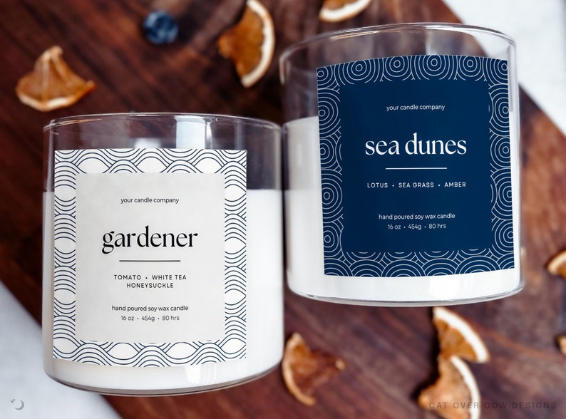 Two candles with custom labels. Left label is beige, right label is navy blue. Both have line art drawing around the edges framing text in the middle. There are custom text fields for the candle company, name, scents, and size.