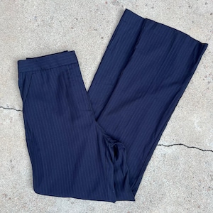 May include: Navy blue pinstripe trousers. The pants are folded and laid out on a concrete surface. The trousers have a classic pinstripe pattern and a tailored fit, suitable for professional or casual wear.