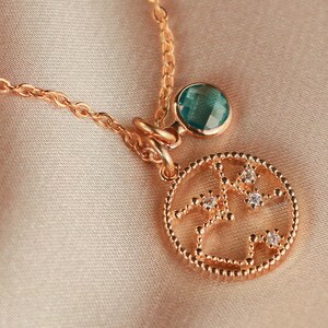 May include: A gold necklace with a round pendant featuring a constellation design with small clear stones. The pendant is attached to a small teal blue gemstone.