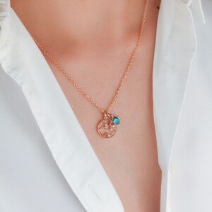 May include: A gold chain necklace with a delicate pendant featuring a circular design with small sparkling stones and a turquoise blue gemstone.