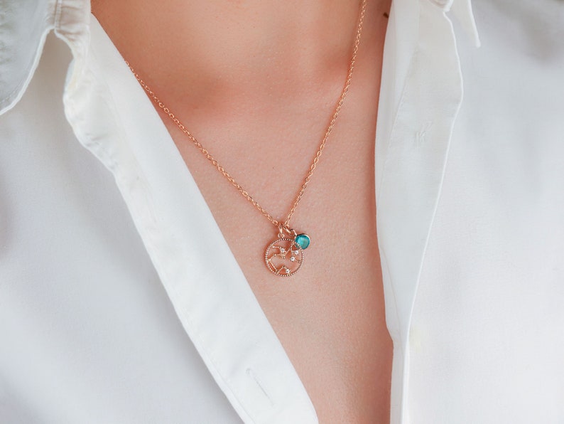 May include: A gold chain necklace with a delicate pendant featuring a circular design with small sparkling stones and a turquoise blue gemstone.