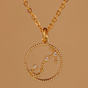 May include: A gold necklace with a circular pendant featuring a constellation of small diamonds in the shape of the Scorpio zodiac sign.