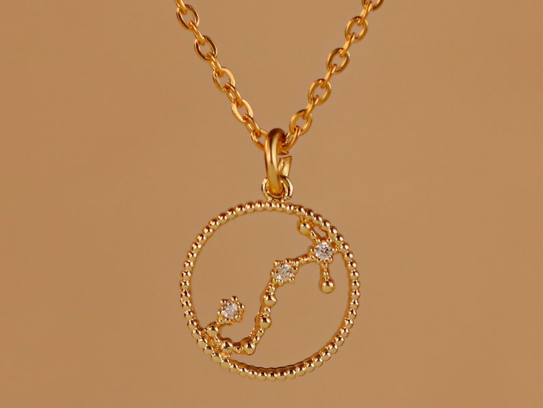 May include: A gold necklace with a circular pendant featuring a constellation of small diamonds in the shape of the Scorpio zodiac sign.