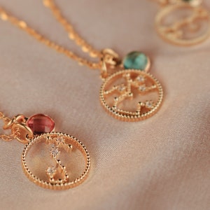 May include: Three gold necklaces with zodiac constellation pendants. Each pendant features a different constellation with a small gemstone in the center. The gemstones are red, green, and blue.