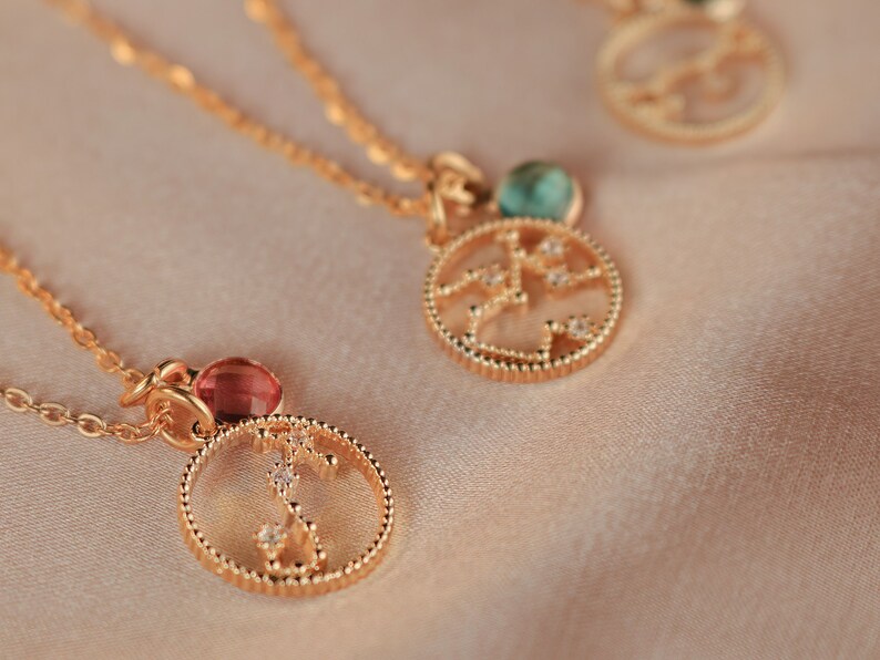 May include: Three gold necklaces with zodiac constellation pendants. Each pendant features a different constellation with a small gemstone in the center. The gemstones are red, green, and blue.
