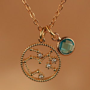 May include: A gold necklace with a pendant featuring a constellation design with small clear stones and a blue gemstone charm.