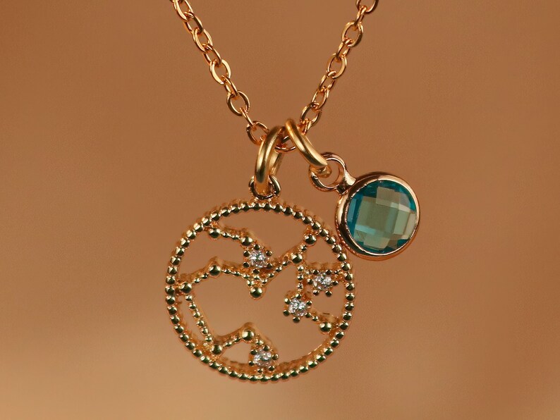 May include: A gold necklace with a pendant featuring a constellation design with small clear stones and a blue gemstone charm.