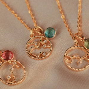 May include: Three gold necklaces with zodiac constellation pendants. Each pendant features a different constellation design with small clear crystals. The necklaces have different colored gemstones: pink, green, and blue.
