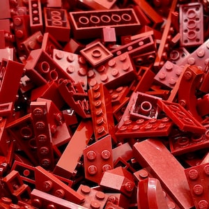 May include: A large pile of red plastic building blocks. The blocks are in various shapes and sizes, including squares, rectangles, and triangles.