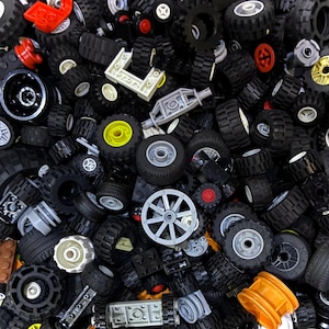 May include: A collection of black toy tires and wheels of various sizes and designs. Some wheels have gray, yellow, or red accents. The image shows a variety of toy car parts, including axles and connecting pieces.