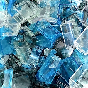May include: A close-up shot of a pile of transparent and translucent plastic building blocks in shades of blue and clear. The blocks are various shapes and sizes, with some appearing to be interlocking pieces.