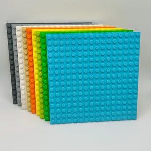 May include: A set of ten Lego baseplates in various colors, including gray, white, tan, orange, yellow, green, and blue. The baseplates are arranged in a stack, with the blue baseplate on the bottom.