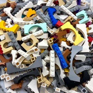 May include: A pile of colorful plastic building blocks in various shapes and sizes. The blocks are in shades of yellow, blue, gray, white, and brown. Some blocks have curved edges, while others are rectangular. The blocks are scattered, creating a playful and creative scene.