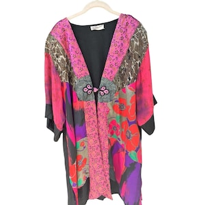 May include: A kimono-style jacket featuring a vibrant patchwork design with bright pink, red, purple, and black panels. The garment includes floral and abstract patterns, a black base, and a single decorative frog closure at the center front.