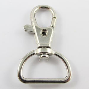 May include: Silver metal swivel clasp with a D-ring. The clasp has a spring-loaded gate and a swivel hook.