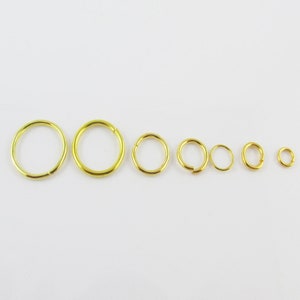 May include: A set of seven gold jump rings of varying sizes. The rings are arranged in a line from largest to smallest.