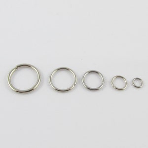 May include: Five silver-coloured, circular hoop earrings of varying sizes are arranged in a row. The hoops are made of a shiny metal and have a simple, minimalist design. The earrings are suitable for ear piercings.