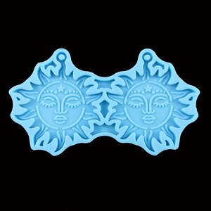 May include: A light blue silicone mould with two sun faces. Each sun has a closed eye, a nose, and a mouth. The sun has a star and dots around the face.