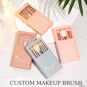 May include: Three rectangular makeup brush cases in peach, light pink, and grey, each featuring a clear window displaying internal brushes and the white printed text "Carlo" with a small heart icon on the front surface of the case.
