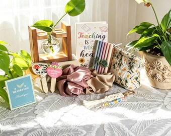 May include: A collection of items including a glass plant propagation bulb in a wooden stand, a notebook with the text Teaching is work heart, a set of pens, two satin scrunchies, a floral embroidered pouch, and a macrame keychain with beads.