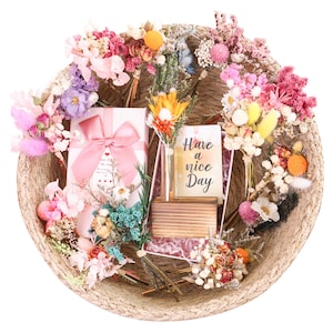 May include: A woven basket filled with colorful dried flowers, a gift box with a pink bow, and a card that reads "Have a nice Day". The arrangement includes various flower types in shades of pink, orange, yellow, and purple.