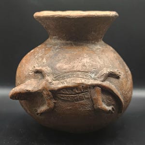 May include: A brown, handcrafted ceramic vase with a rounded body and a flared rim. The vase features a detailed relief of a turtle encircling the body. The vase is approximately 6 inches tall.