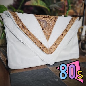May include: White leather clutch with a chevron design in snakeskin and white. The clutch has a flap closure and a rectangular shape. The image includes a graphic that says "80s".