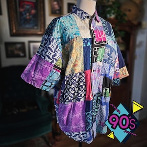 May include: A short-sleeved button-down shirt featuring a patchwork design composed of various fabric squares in shades of purple, blue, black, white, and yellow. The shirt displays diverse patterns including geometric shapes, floral motifs, and abstract lines.
