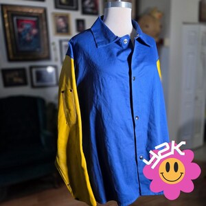 May include: A blue button-up jacket with yellow sleeves. The jacket has a collared neckline and a small pocket on the left sleeve. A pink flower graphic with the text "Y2K" is on the lower right.