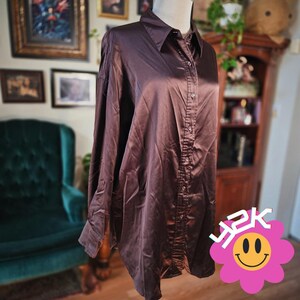 May include: A long-sleeved button-down shirt in a dark brown satin fabric with a pointed collar and a full-length front button placket. The shirt features a smooth, reflective finish and a straight hemline, presented in a solid, deep chocolate brown color.