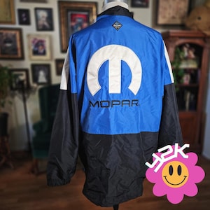 May include: A blue, black, and white MOPAR jacket. The back of the jacket features a large white MOPAR logo and the word "MOPAR" in black. The jacket has a black collar and sleeves, with white accents on the shoulders.