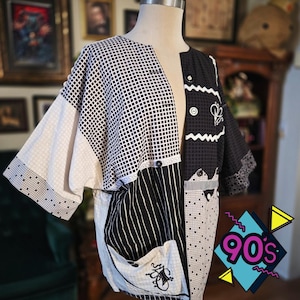 May include: A patchwork jacket with a 90s theme. The jacket features a mix of black and white patterns, including checkered, striped, and geometric designs. It has a button-up front and pockets. The sleeves are wide and the overall style is vintage.