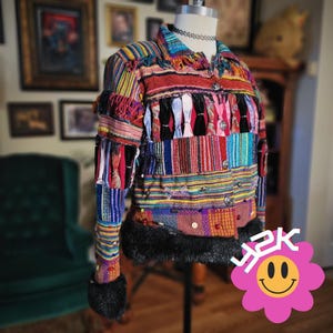 May include: A colorful patchwork jacket with a variety of textures and patterns. The jacket features a mix of striped, woven, and embellished fabrics in shades of red, blue, yellow, and green. It has a black fur trim and decorative buttons.