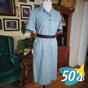 May include: A vintage-style dress in blue and green gingham check pattern. The dress features short sleeves, a collared neckline, and a black belt. The dress has a fitted bodice and a knee-length skirt. The image also includes the text "50's".