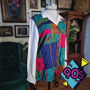 May include: A vintage button-down shirt with a white collar and sleeves. The shirt's front features a colorful patchwork design in teal, pink, orange, and blue. The shirt is displayed on a mannequin. The image includes a 90s graphic.