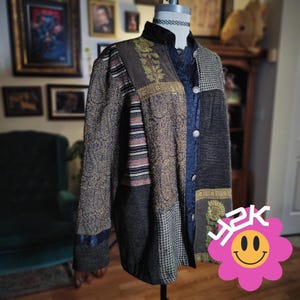 May include: A patchwork jacket with a variety of textures and patterns. The jacket features a mix of fabrics, including paisley, houndstooth, and striped panels. It has a high collar and button closure. The color palette includes shades of brown, gray, and blue.